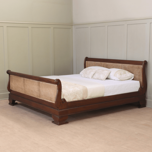 Wooden sleigh bed with wicker headboard in a room with panelled walls.