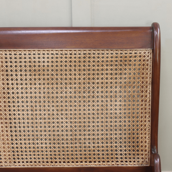 Close-up of a wooden headboard with wicker detailing against a plain wall.